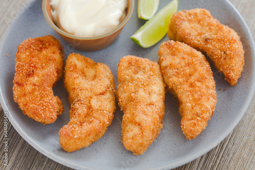 Homemade crispy fried breaded fish sticks or fish fingers made from self-caught triggerfish fillet, served on plate with mayonnaise and lime slices (Selective Focus, Focus in the middle of the image)