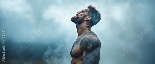 Muscular man with tattoos gazes upward into cloudy sky, breathing smoke