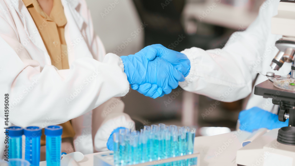 Two Asian female scientists wearing laboratory gloves sit at a table, carefully examining a test tube filled with blue liquid, using a microscope for detailed analysis in a research laboratory