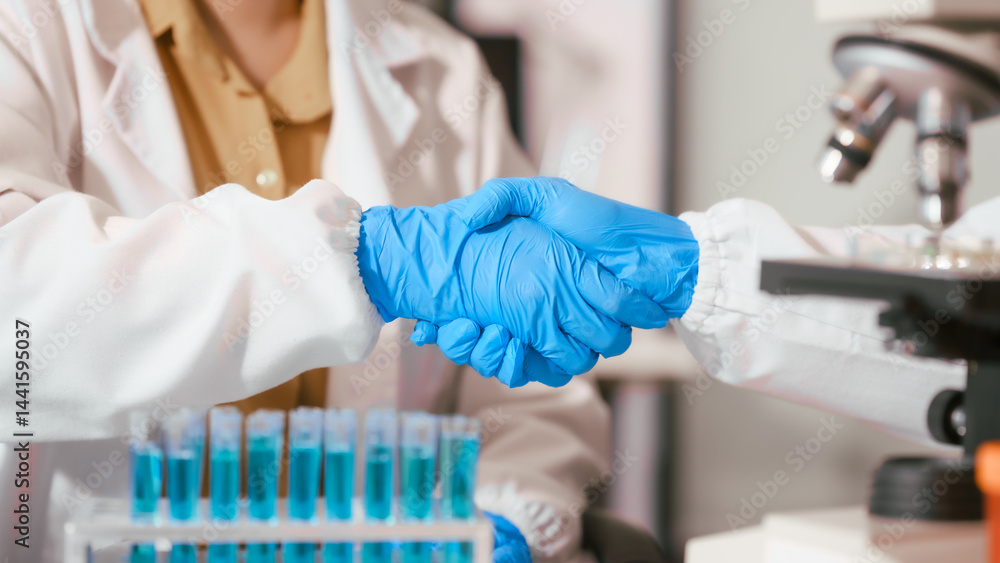 Two Asian female scientists wearing laboratory gloves sit at a table, carefully examining a test tube filled with blue liquid, using a microscope for detailed analysis in a research laboratory