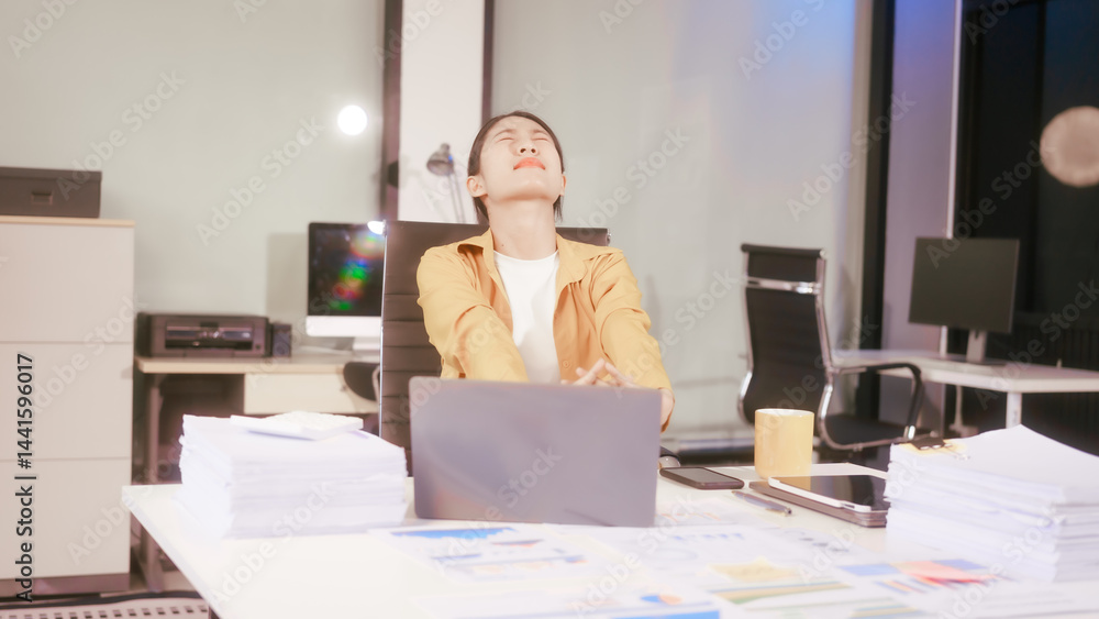 An Asian woman works at her office desk, feeling stressed and experiencing pain from sitting for a long time, struggling with discomfort and fatigue while trying to stay focused on her tasks.