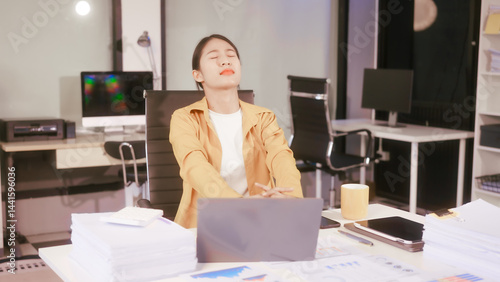 Obraz na płótnie An Asian woman works at her office desk, feeling stressed and experiencing pain from sitting for a long time, struggling with discomfort and fatigue while trying to stay focused on her tasks. w salonie