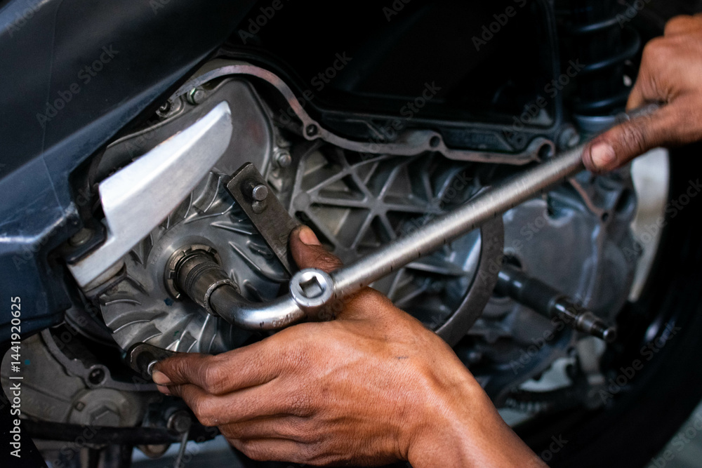 Close-up of a mechanic's hands working on a scooter's CVT transmission system, focusing on the front pulley shaft during maintenance Close-up of a mechanic's hands working on a scooter's CVT transmission system, focusing on the front pulley shaft during maintenance