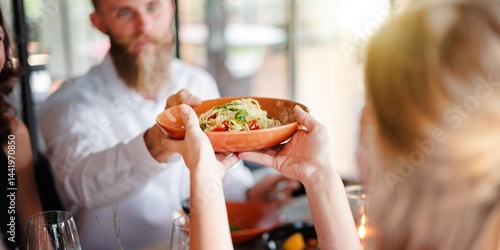 Obraz na plátne A person hands a bowl of pasta to another at a dining table