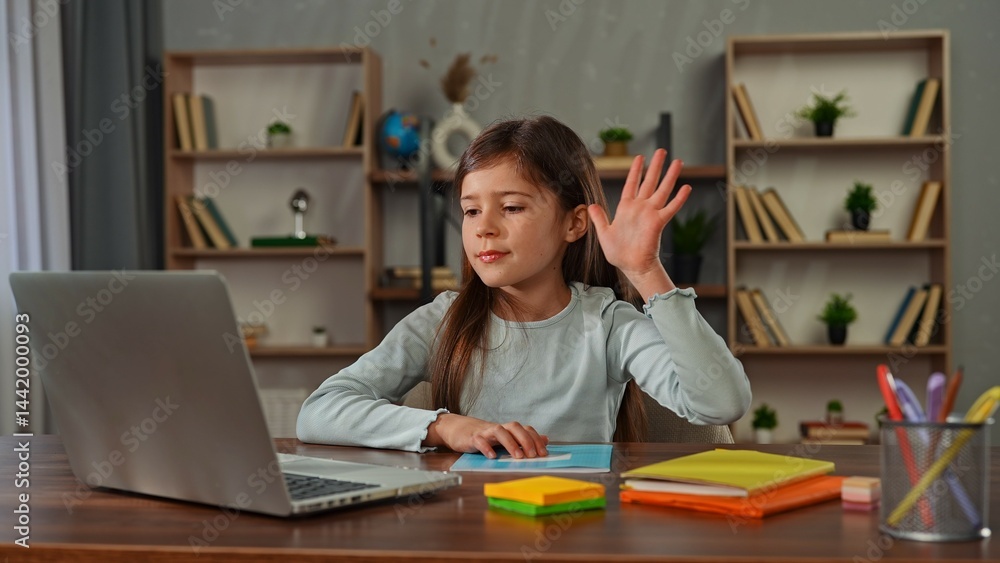 Young child girl studying at home, small girl sits at desk and attends school class online on laptop, doing homework, greeting teacher, looks at camera. Young child girl studying at home, small girl sits at desk and attends school class online on laptop, doing homework, greeting teacher, looks at camera.