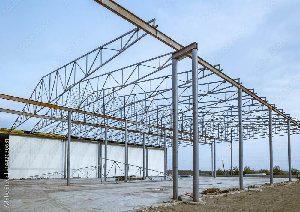 Fototapeta premium Installation of a steel frame under the sip panels of a warehouse with refrigeration chambers. Beams and roof rafters are mounted on the bearing supports. Foundation and concrete floor. Skeleton roof