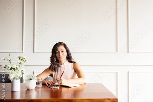 Young hispanic woman writing at a table. Woman with long hair writing notes. Woman at table with a notebook. Woman writing in a journal. Professional marketing execustive taking notes in an agenda.
