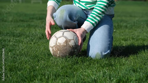 Unrecognizable person crouched on the grass holding a ball against the background of grass stains on the knees of jeans. Spoiled clothes. Concept of daily stains on clothes