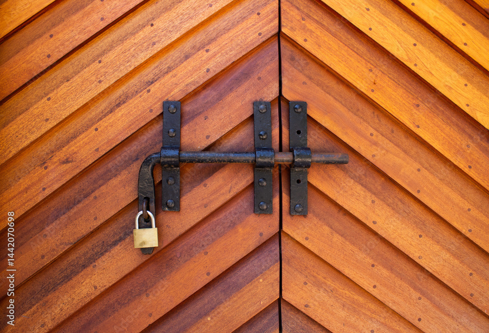 Wooden door with metal latch and padlock - architectural texture. Chevron pattern wooden gate with vintage bolt and lock. Wooden door with metal latch and padlock - architectural texture. Chevron pattern wooden gate with vintage bolt and lock.