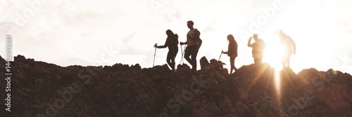 Silhouettes of hikers on a rocky ridge at sunset. Group of hikers with walking sticks. Adventure and exploration in nature. Hiking and trekking enthusiasts. Hiking adventure on mountain trail.