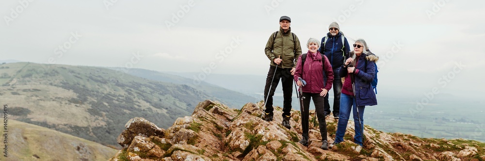 A diverse senior group of four hikers stand on a rocky peak. The hikers, dressed for the outdoors, enjoy view of the mountains and valleys. Happy senior group with hiking dressed at a rocky peak A diverse senior group of four hikers stand on a rocky peak. The hikers, dressed for the outdoors, enjoy view of the mountains and valleys. Happy senior group with hiking dressed at a rocky peak