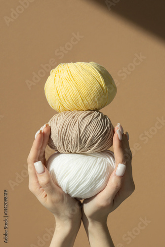 Three balls of knitting thread in women's hands on a brown insulated background in sunlight. Vertical frame.
