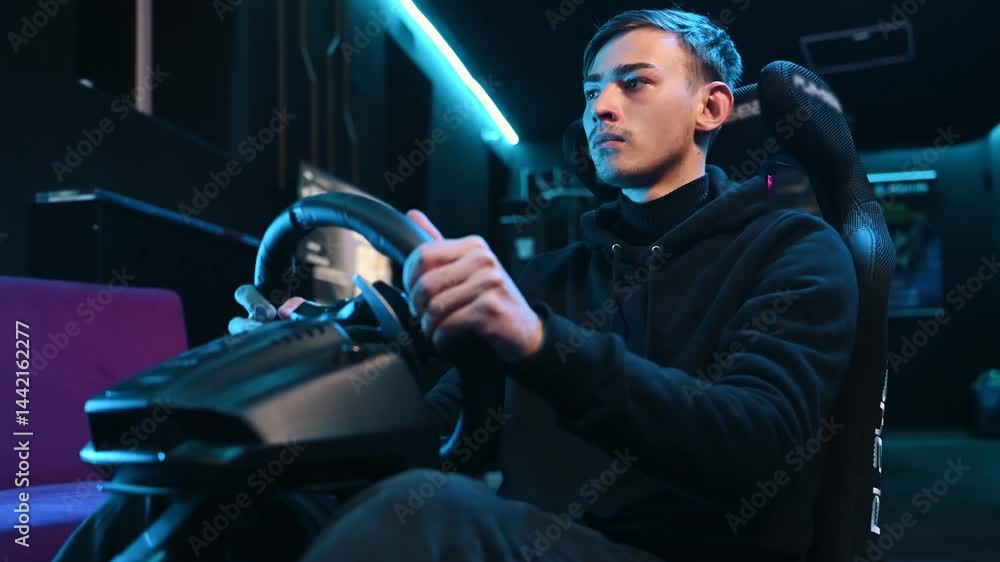 In the seat. Young guy is playing racing game by using driving simulator.