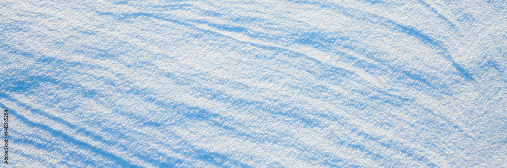 Beautiful winter background with snowy ground. Natural snow texture. Wind sculpted patterns on snow surface. Wide panoramic texture for background and design.
