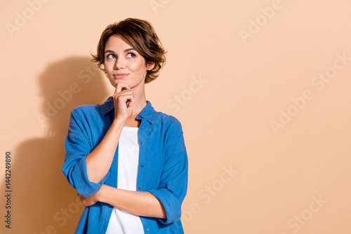 Obraz na płótnie Portrait of young pensive clever lady in blue shirt touch chin looking empty space deep thinking isolated on beige color background w salonie