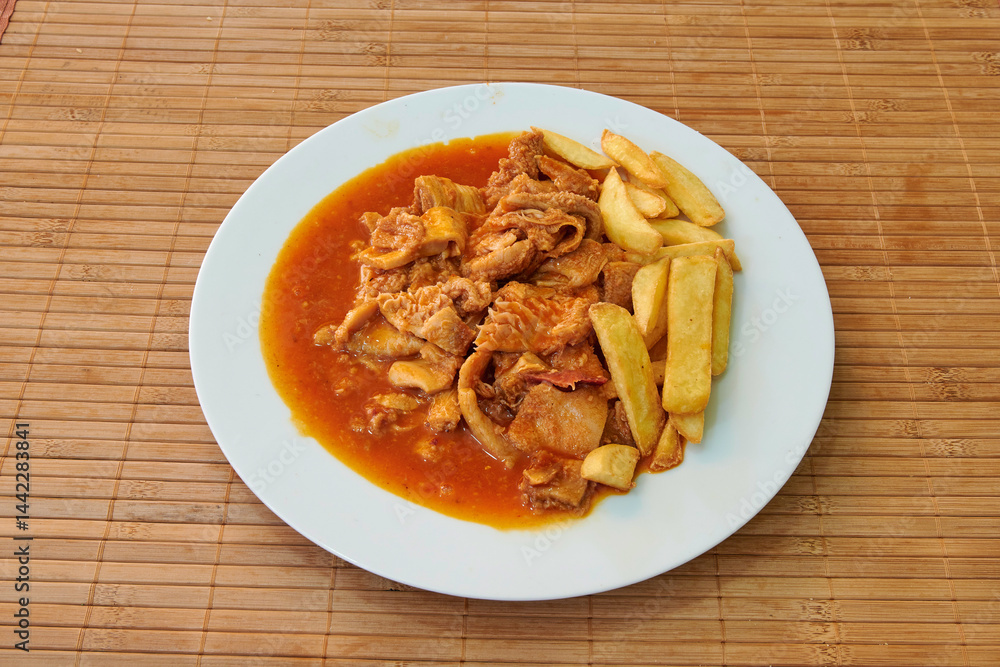 A plate of food with meat and potatoes. The meat is covered in sauce and the potatoes are cut into small pieces