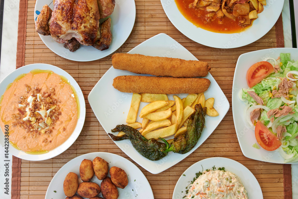 A table with a variety of food including chicken, potatoes, and salad. There are also some bowls and plates on the table