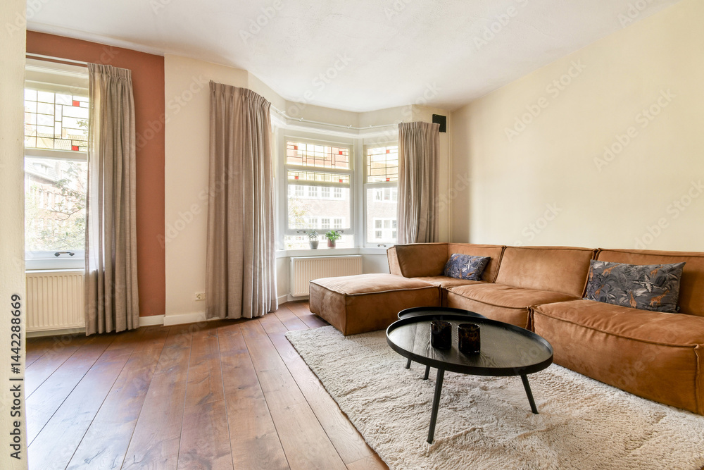 Fototapeta premium A bright and inviting living room featuring large windows, soft curtains, and comfortable seating that embodies a warm ambiance for relaxation.