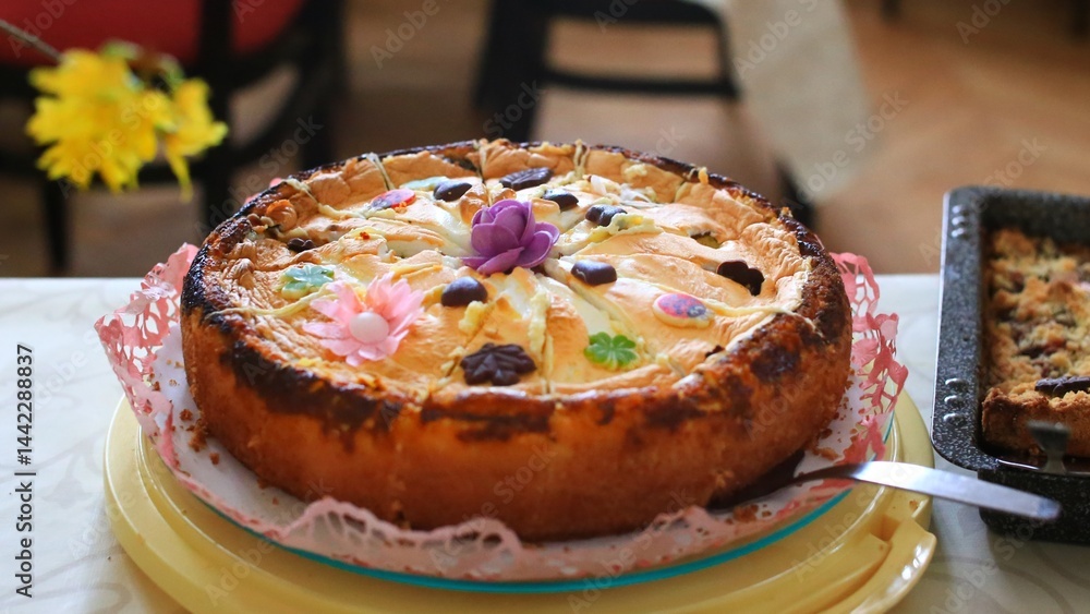 Decorated apple cake with chocolate and sugar flowers on a table with another baked pastry