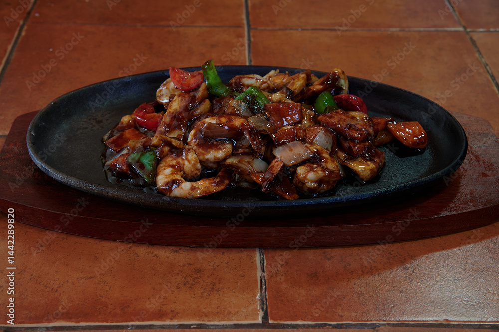 A plate of food with meat and vegetables on a wooden board. The plate is on a table