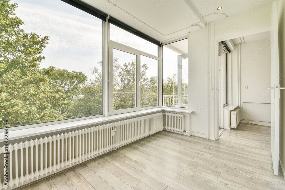 Fototapeta premium Spacious room featuring large windows that allow natural light to flood in, highlighting the beautiful wooden flooring and minimalistic design.