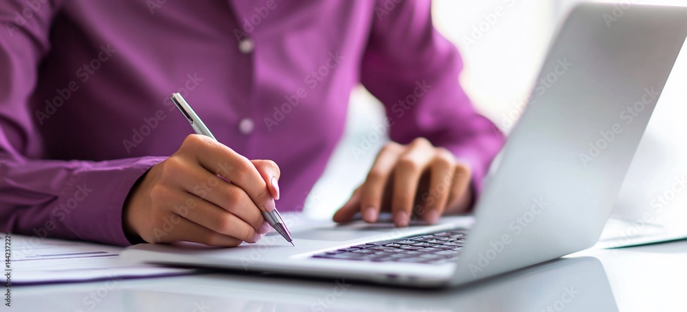 Close-up of a person's hands writing on a document near a laptop.