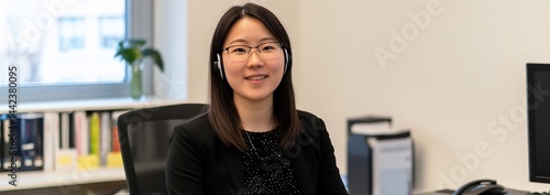 Obraz na płótnie Smiling Asian woman in headset at office desk. w salonie