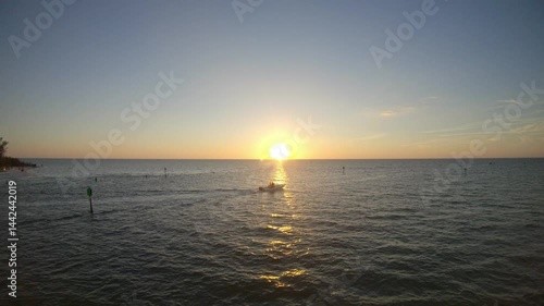 A small boat sailing out from a beach in Naples, Florida with the sun setting over the sea.