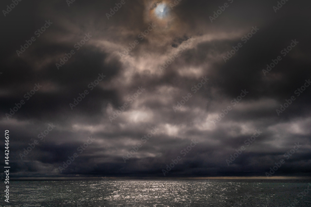 Sun between dark storm clouds over ocean. Dramatic seascape. Clouds and rain flurry over sea.