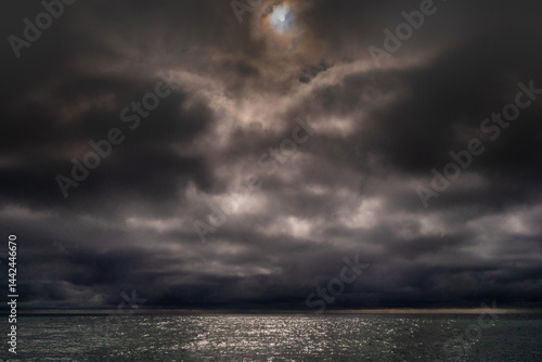 Obraz na płótnie Sun between dark storm clouds over ocean. Dramatic seascape. Clouds and rain flurry over sea. w salonie