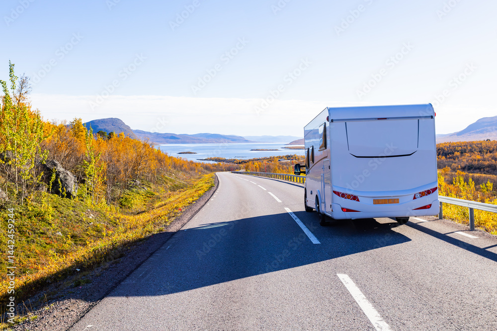 Motorhome driving on a scenic road in Kiruna, Sweden, with autumn foliage and beautiful lake views.