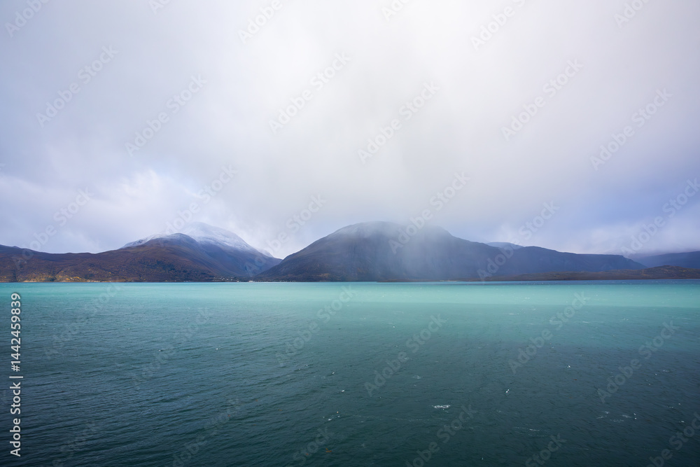 Autumn landscape of the Lyngen Alps in Northern Norway with snowy peaks, dramatic clouds, and a tranquil fjord.