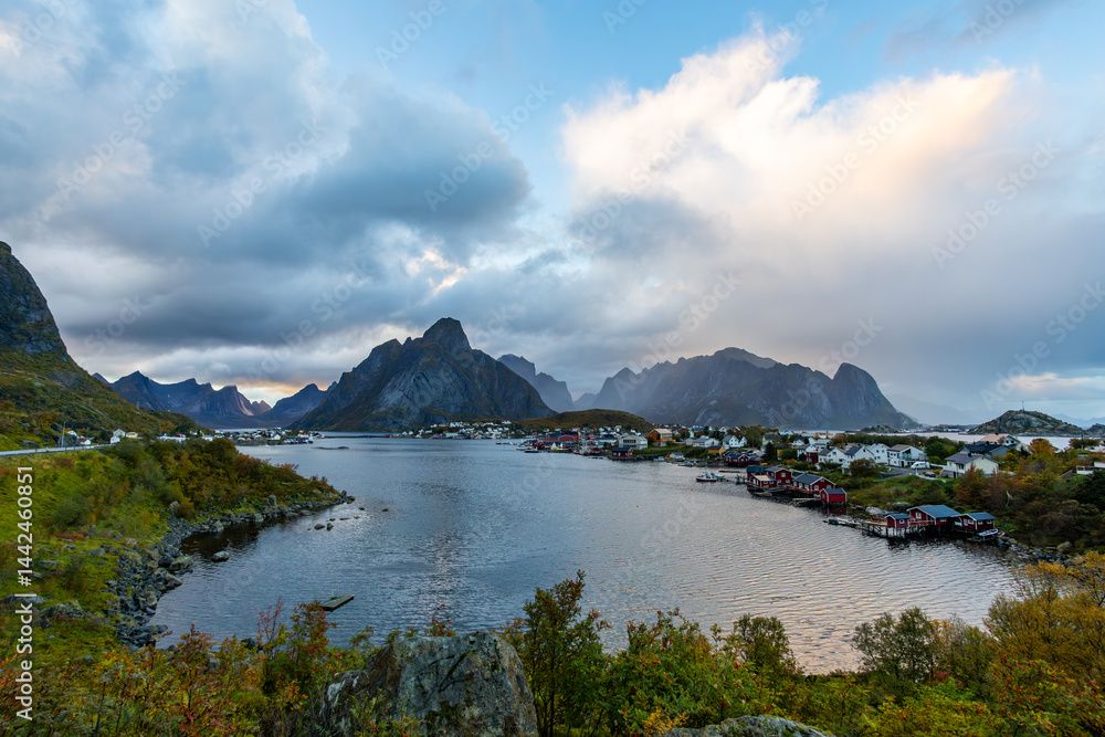 Autumn sunset in Reine, Lofoten Islands, Norway, with dramatic mountains, calm waters, and traditional houses along the shore.