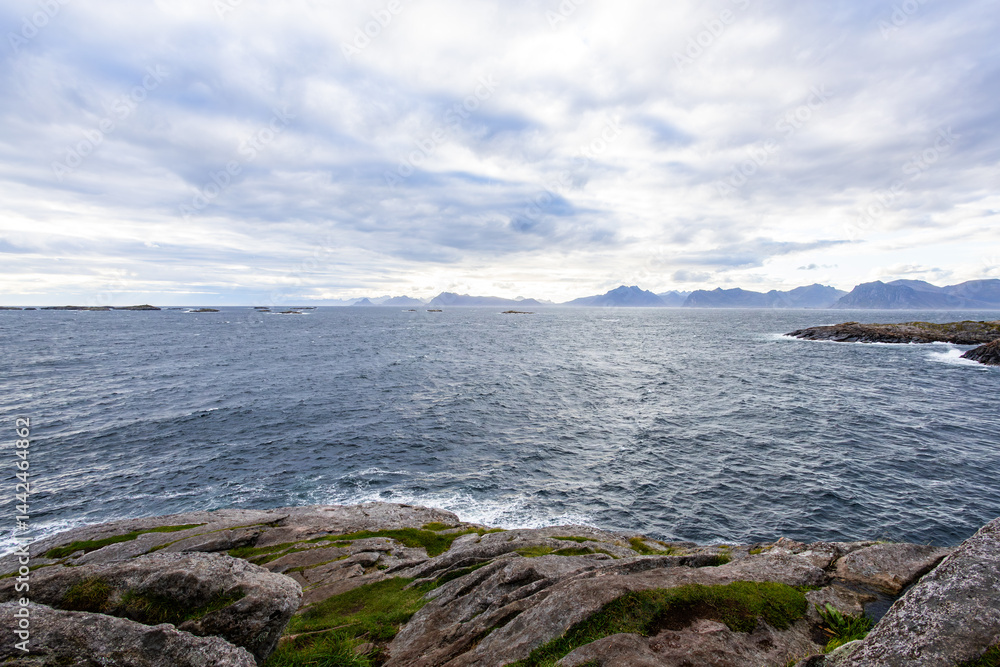 A scenic view of Henningsvær in Lofoten Islands, northern Norway, showcasing traditional buildings along the harbor with mountains in the background.