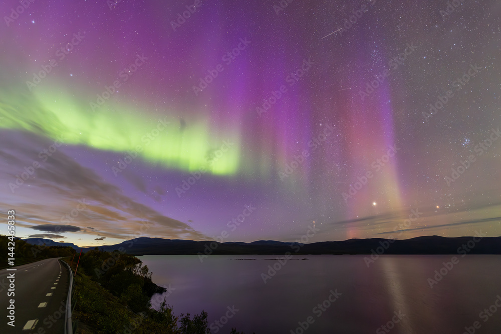 Northern lights in Kiruna, Sweden, reflecting on calm water in September with stars and forest in the background.