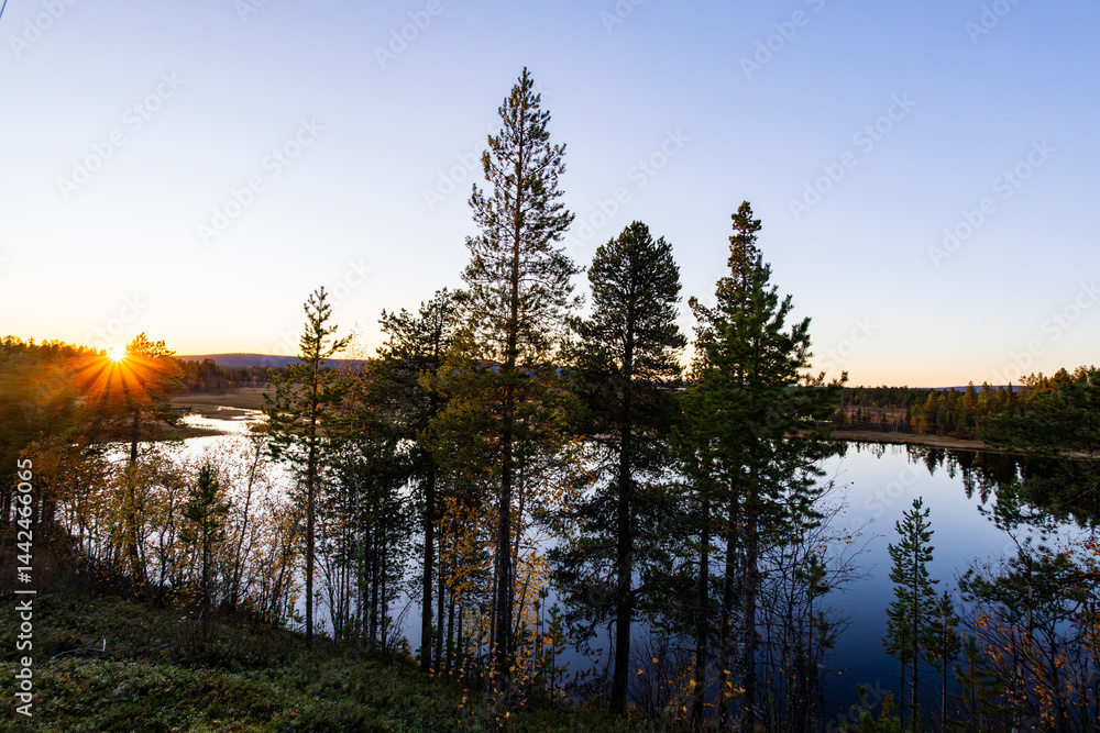 A peaceful sunset over a lake in Lapland, Sweden, with the reflection of trees in the still water.