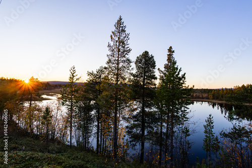 Obraz na płótnie A peaceful sunset over a lake in Lapland, Sweden, with the reflection of trees in the still water. w salonie