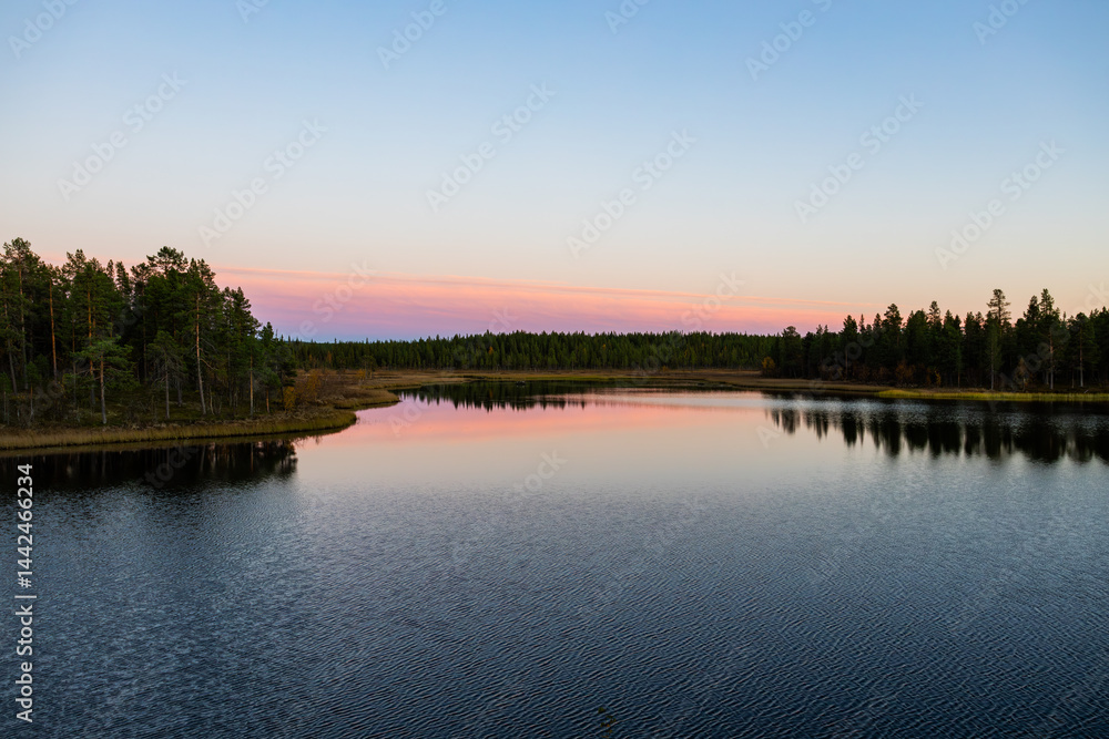 A peaceful sunset over a lake in Lapland, Sweden, with the reflection of trees in the still water.