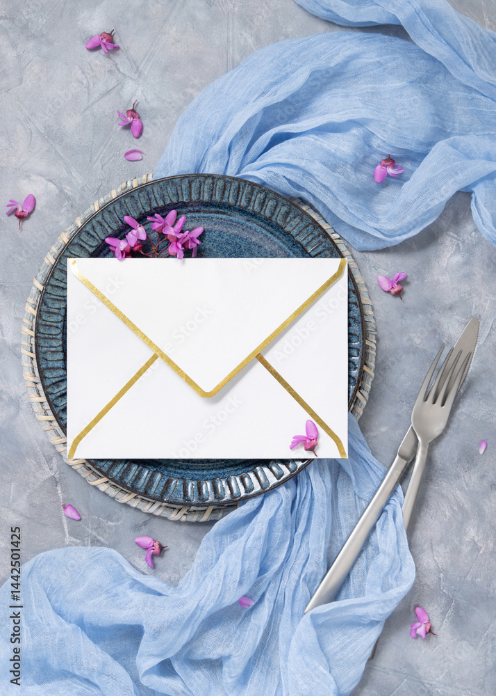 Wedding table place with envelope near fabric and wild purple flowers top view on gray, mockup