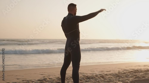 A surfer warming up on the beach before entering the water for a surf session during a beautiful golden sunset.