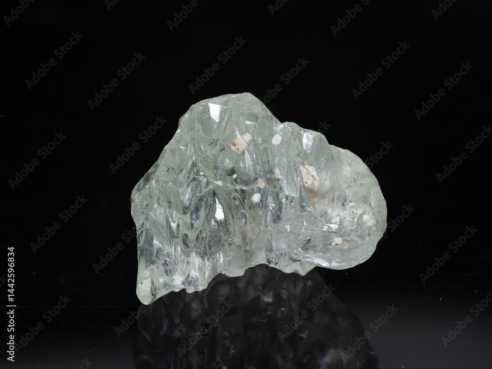 A transparent, light green beryl crystal sits prominently on a dark, rocky base with internal inclusions visible, displaying angular facets and a somewhat uneven, natural shape