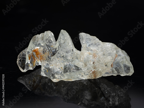 Obraz na płótnie A stunning, transparent natural beryl crystal specimen showcasing a complex, jagged structure with internal inclusions of reddish-brown minerals against a black reflective surface w salonie