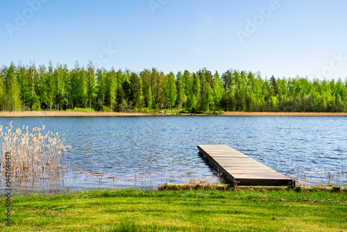 Lake and dock in Finland. Wood pier. Finnish nature landscape. Beautiful summer day. Water and blue sky. Forest in the background. Grass beach in vacation cottage.