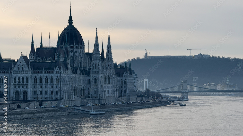 Naklejka premium Majestic view of the Budapest Parliament by the Danube River, capturing European architecture and travel inspiration, perfect for holiday postcards