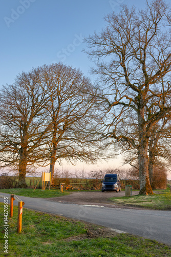 Obraz na płótnie Van parked near picnic area in countryside at sunset under bare trees w salonie