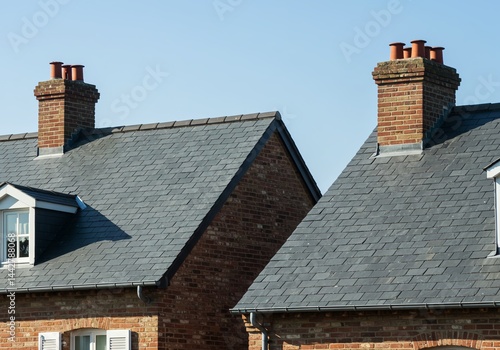 Close-up view of the slate roofs and brick chimneys of two buildings against a clear blue sky.