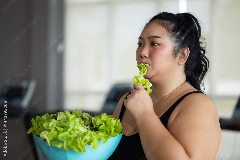 enjoying tasty vegetable salad. beautiful young chubby overweight woman wearing sporty fitness clothes doing exercise indoors at gym fitness sport club, body and health care