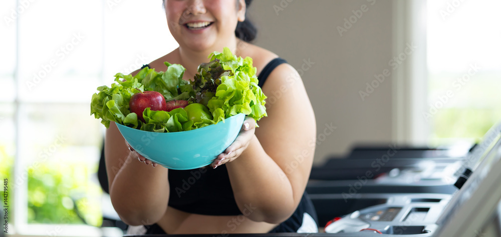Portrait fat woman enjoying eating vegetable salad. beautiful young chubby overweight woman wearing sporty fitness clothes doing exercise indoors at gym fitness sport club, body and health care