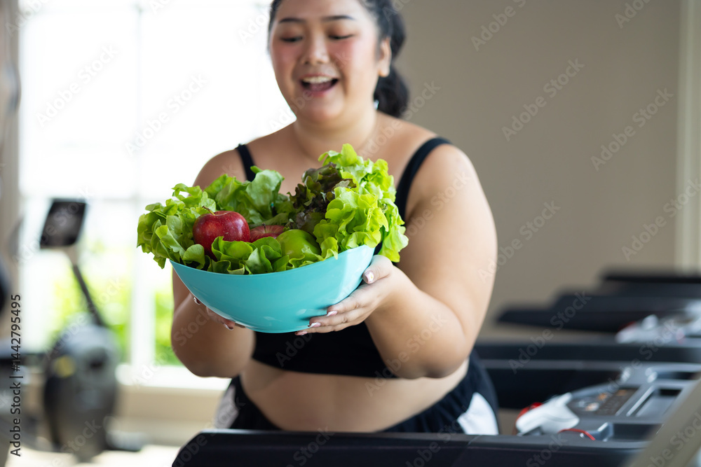 Portrait fat woman enjoying eating vegetable salad. beautiful young chubby overweight woman wearing sporty fitness clothes doing exercise indoors at gym fitness sport club, body and health care