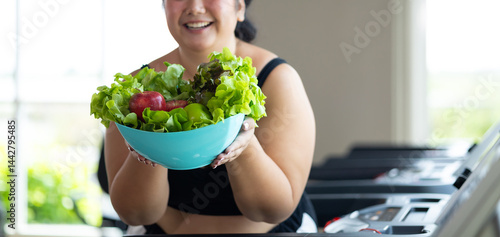 Portrait fat woman enjoying eating vegetable salad. beautiful young chubby overweight woman wearing sporty fitness clothes doing exercise indoors at gym fitness sport club, body and health care